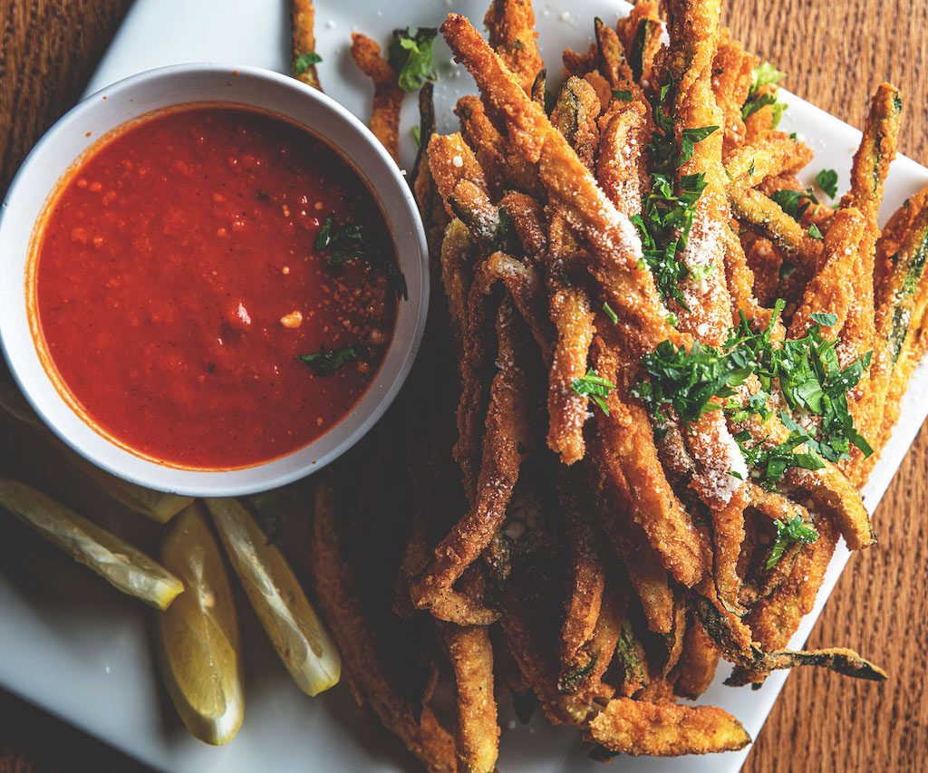 Crispy zucchini sticks served on a white plate with a side of marinara sauce, showcasing golden-brown breaded zucchini slices, offering a delicious and satisfying appetizer option at Spumoni Gardens.