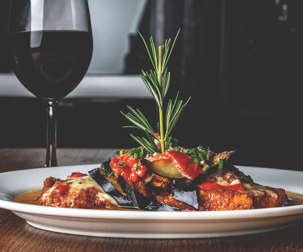 A delicious serving of eggplant Parmesan, featuring slices of eggplant coated in breadcrumbs, fried to a golden brown, layered with marinara sauce and melted mozzarella cheese, presented on a white plate, offering a classic and satisfying Italian dish at Spumoni Gardens.